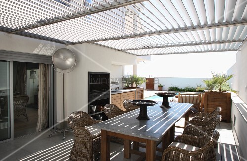 Rattanstühle um Holztisch auf mit Sonnenschutzlamellen überdachter