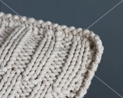 A knitted cushion with an offset ribbed pattern and a crocheted edge (detail)...