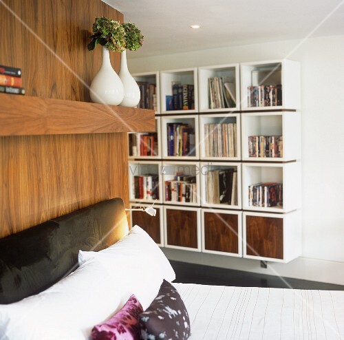 Bett mit gepolstertem Kopfteil vor Holzwand und zeitgenössisches Regal
