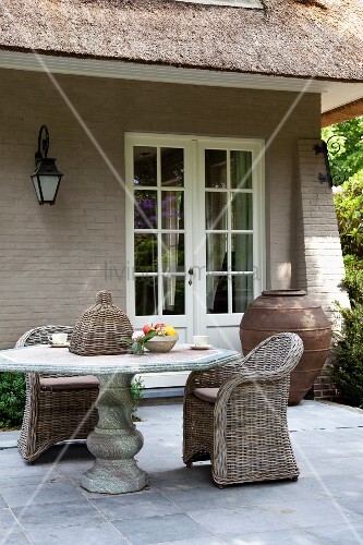Steintisch und Korbstühle auf Terrasse vor Landhaus – Bild kaufen