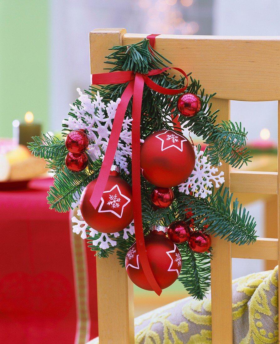 Fir branch with baubles and stars tied to chair back
