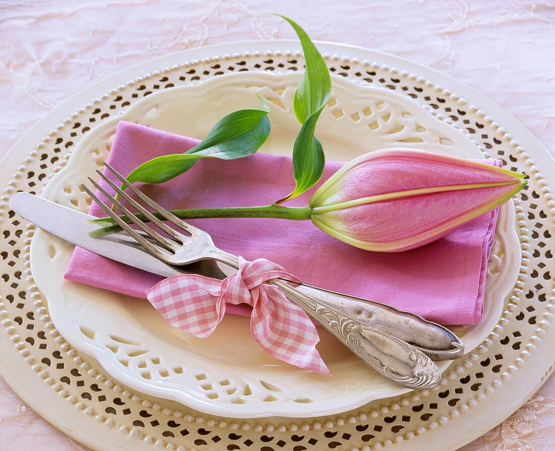 Rosa Serviette mit Lilienknospe auf weißem Teller