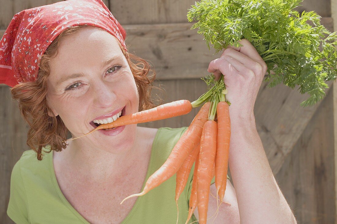 Junge Frau beisst in frisch gepflückte Karotten