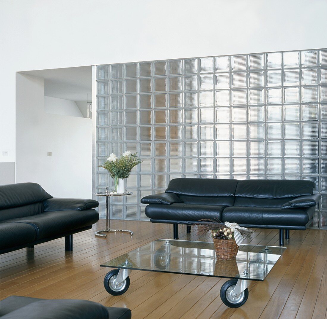 Wohnzimmer mit Sofas und Glastisch auf Rollen vor Glassteinwand