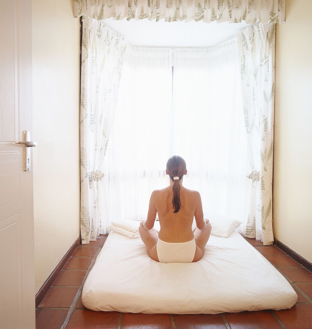 Meditierende Frau auf einer Bettmatratze im kleinen Zimmer mit Ercker