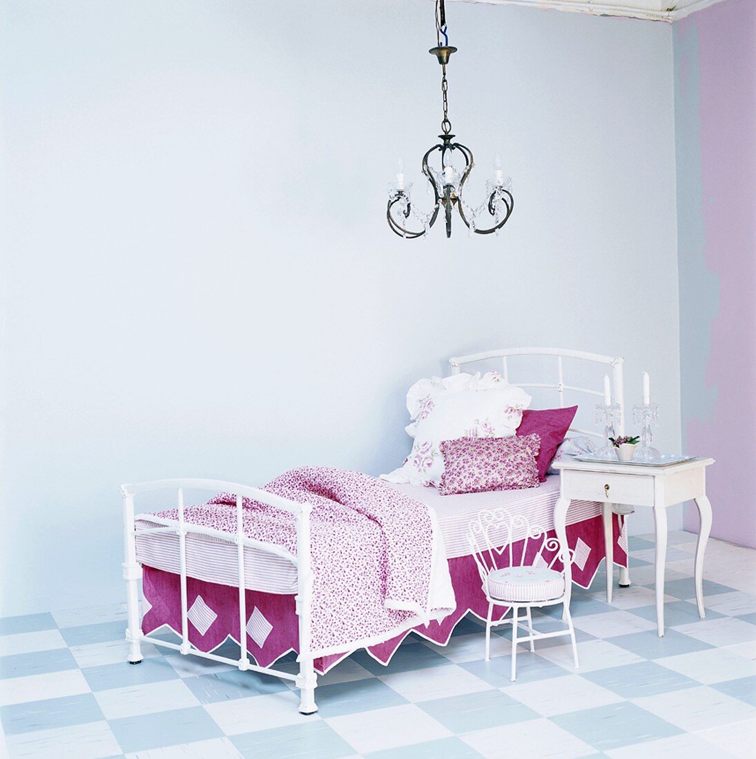 Schmiedeeisernes Einzelbett mit pink-weißer Bettwäsche und Nachttisch unter Kronleuchter