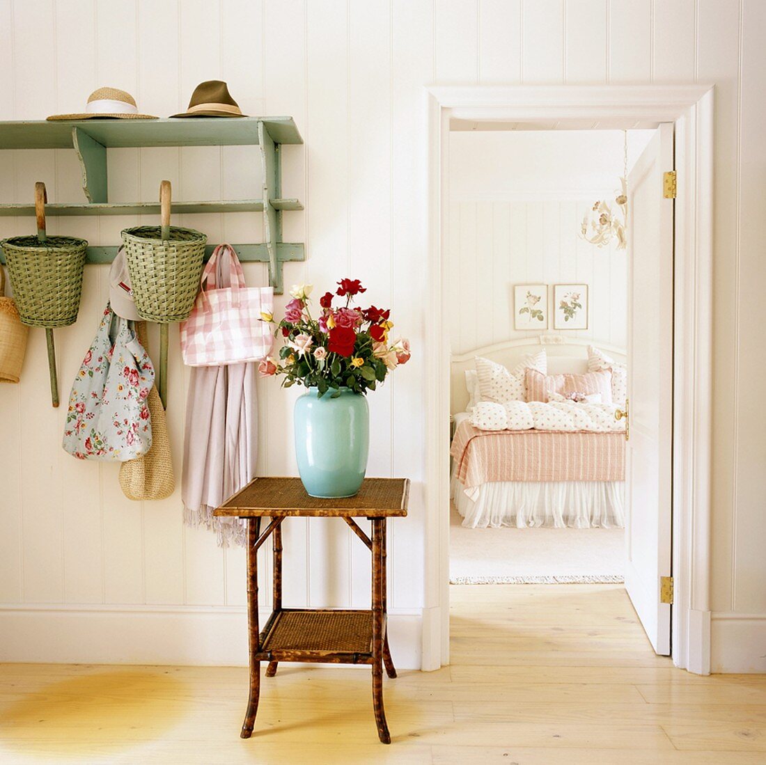 Blick durch Eingangsbereich mit Holztischen und Blumenstrauß in ein romantisches Schlafzimmer