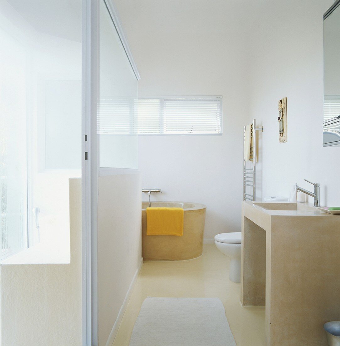 Ein helles Badezimmer mit Glastrennwand und runder Badewanne unter Fenster