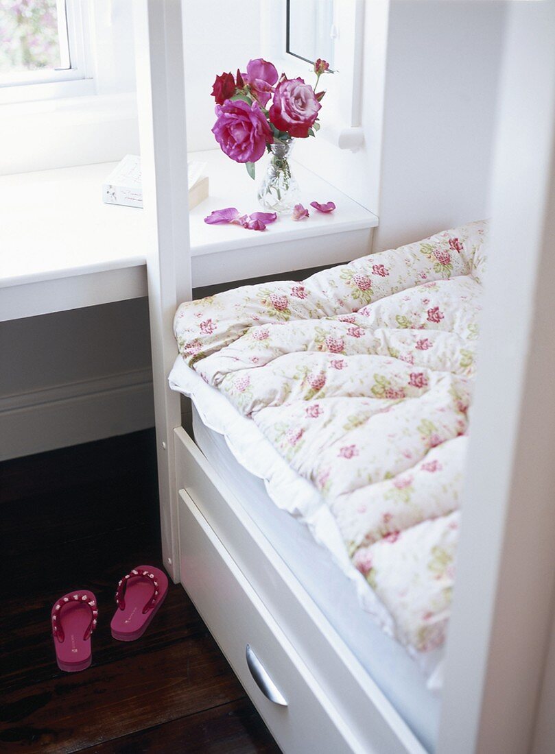 Pinke Flip-Flops neben Einzelbett mit geblümter Bettdecke und Stauraum unter dem Bett