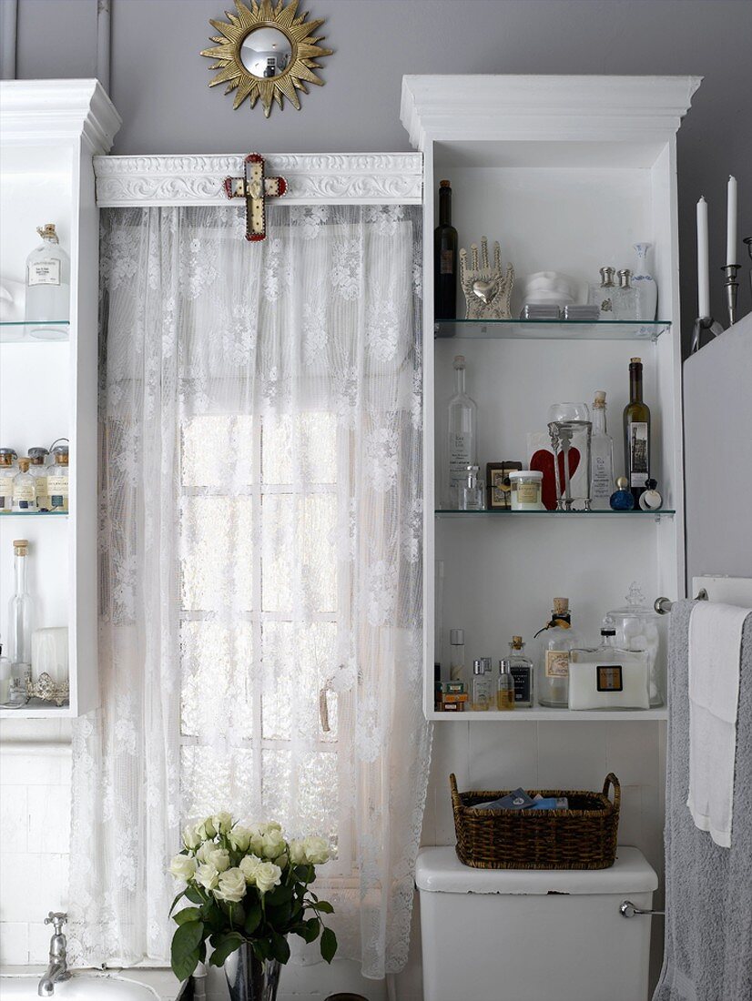 Fenster mit weißen Vorhang zwischen zwei offene Hängeschränke mit Kosmetikutensilien