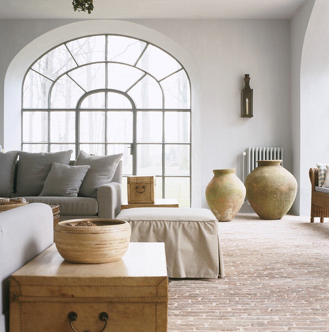 Ein helles Wohnzimmer mit grauer Couchgarnitur vor großes Rundbogenfenster und Backsteinboden