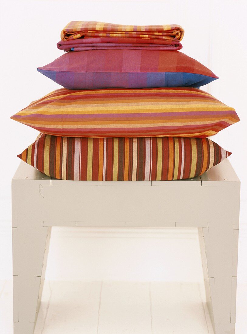 A pile of colourful cushions on a stool