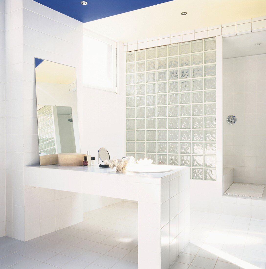 Bad mit gemauertem Waschtisch, angelehntem Badezimmerspiegel und einer Trennwand aus Glasbausteinen