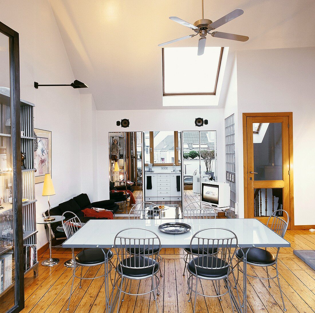 Dining room with ceiling fan above metal table and chairs; two cupboards with mirrored fronts flanking kitchen doorway