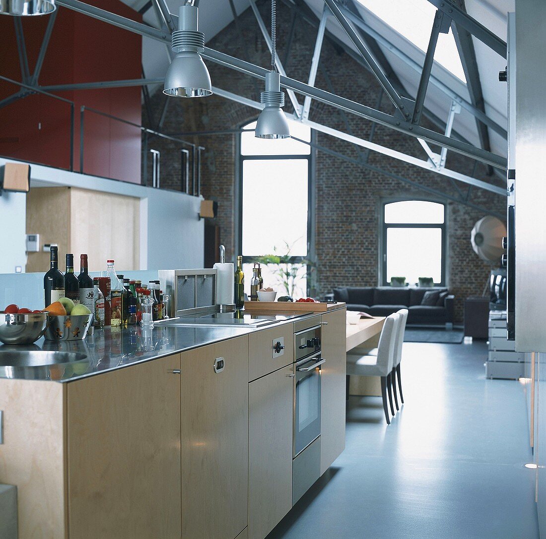 Kitchen area in high-ceilinged, open-plan interior with brick wall and gable ceiling