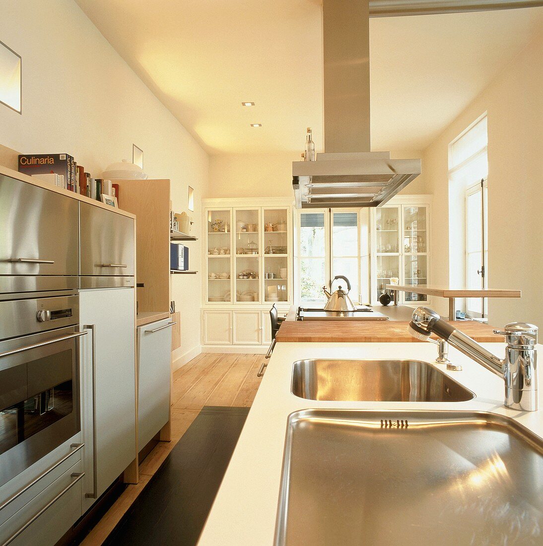 Moderne, gut ausgestattete Küche mit Vitrinenschränken im Hintergrund und Küchengeräten mit Edelstahlfronten