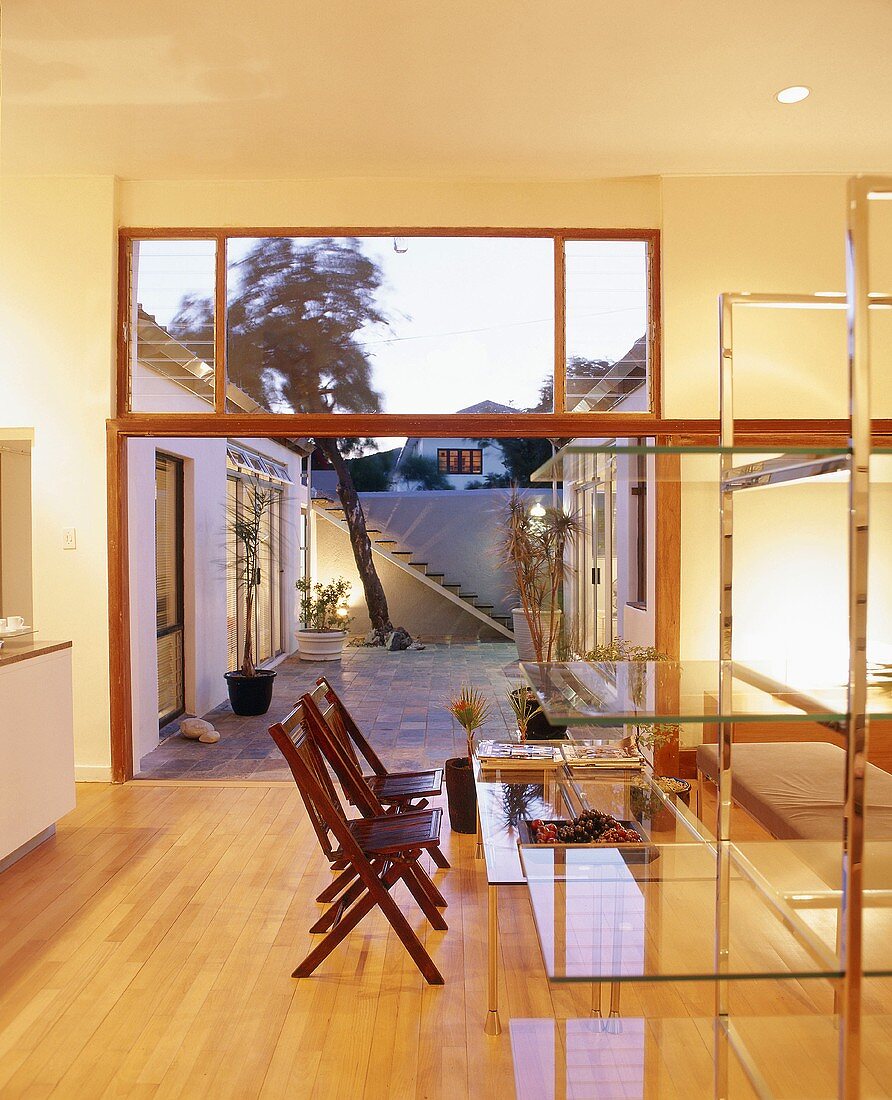 Blick vom erleuchteten Esszimmer mit Glasregal und Glastisch in den abendlichen Innenhof
