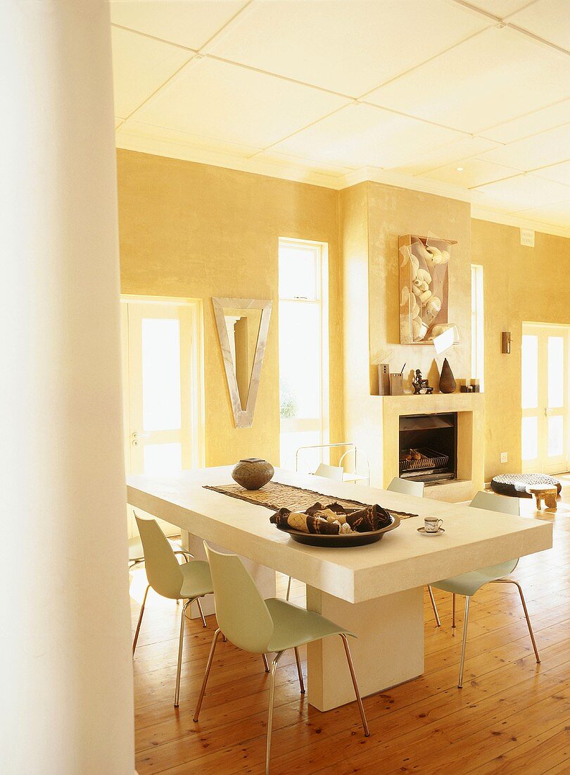 Heavy, white dining table and simple shell chairs in yellow dining room with open fireplace