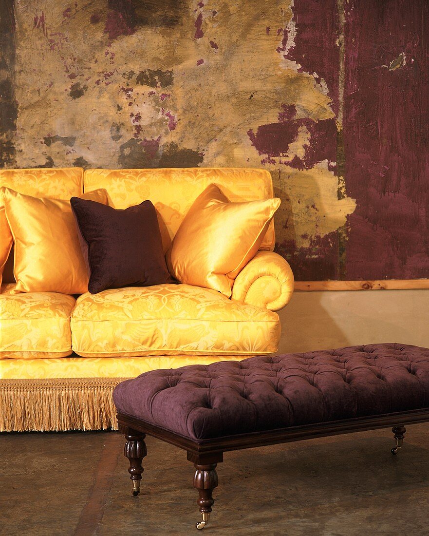 Gold couch with shiny scatter cushions behind ottoman and modern painting with wooden frame on wall