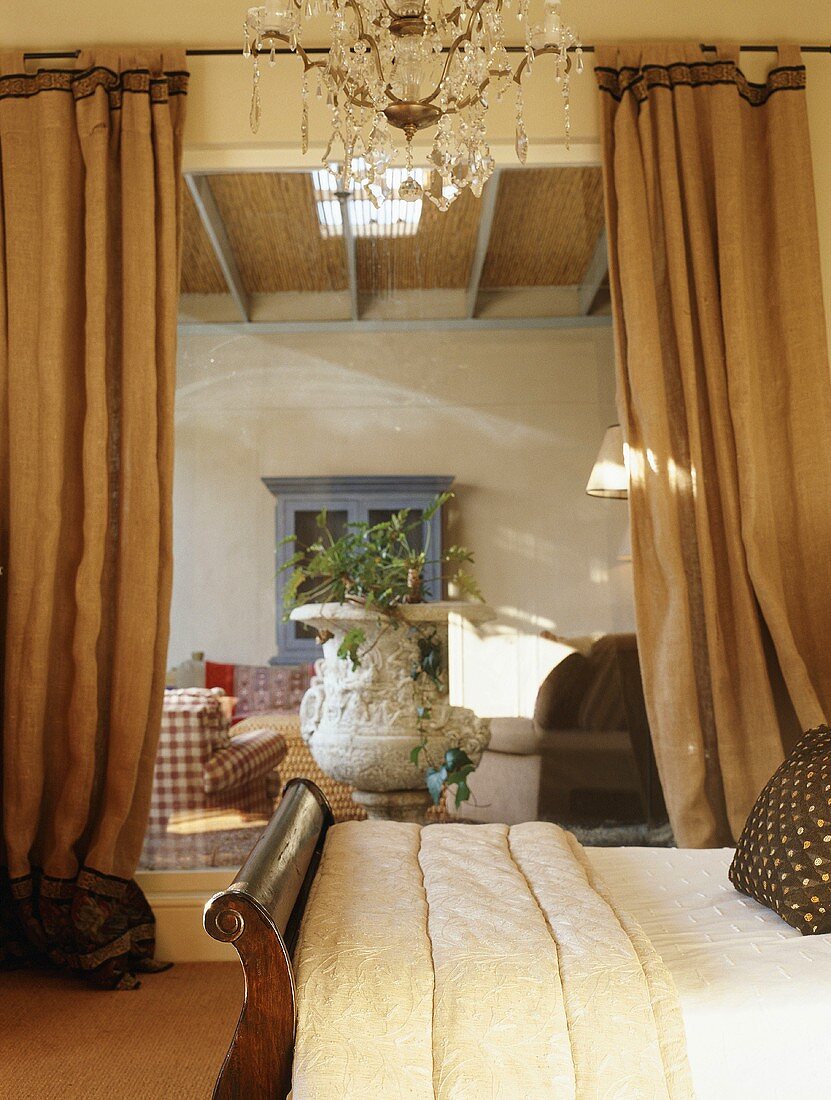 Bedroom with chandelier and view into living room between two heavy curtains