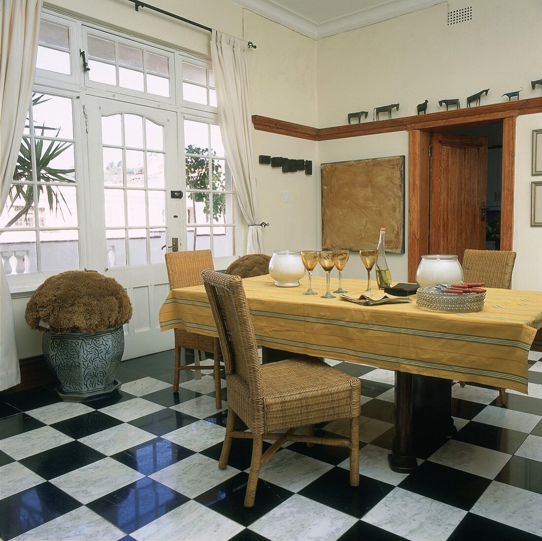 Esszimmer mit Marmorfliesen im Schachbrettmuster, einem großen Esstisch mit Tischdecke und Körbstühlen