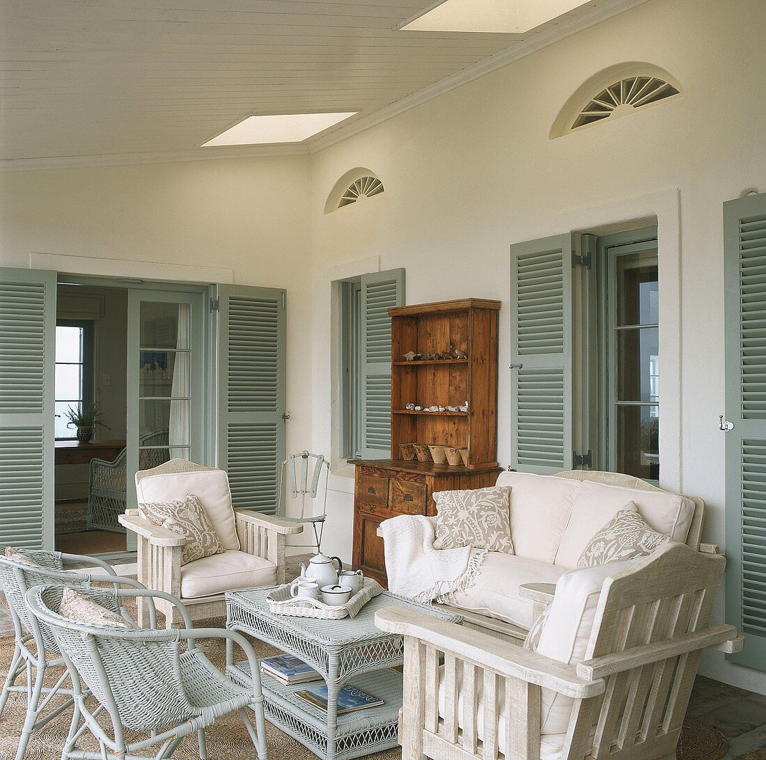 Überdachte Terrasse mit Oberlicht, mit gemütlichen Gartenmöbeln mit weissen Polstern und Kissen und einem Korb-Teetisch