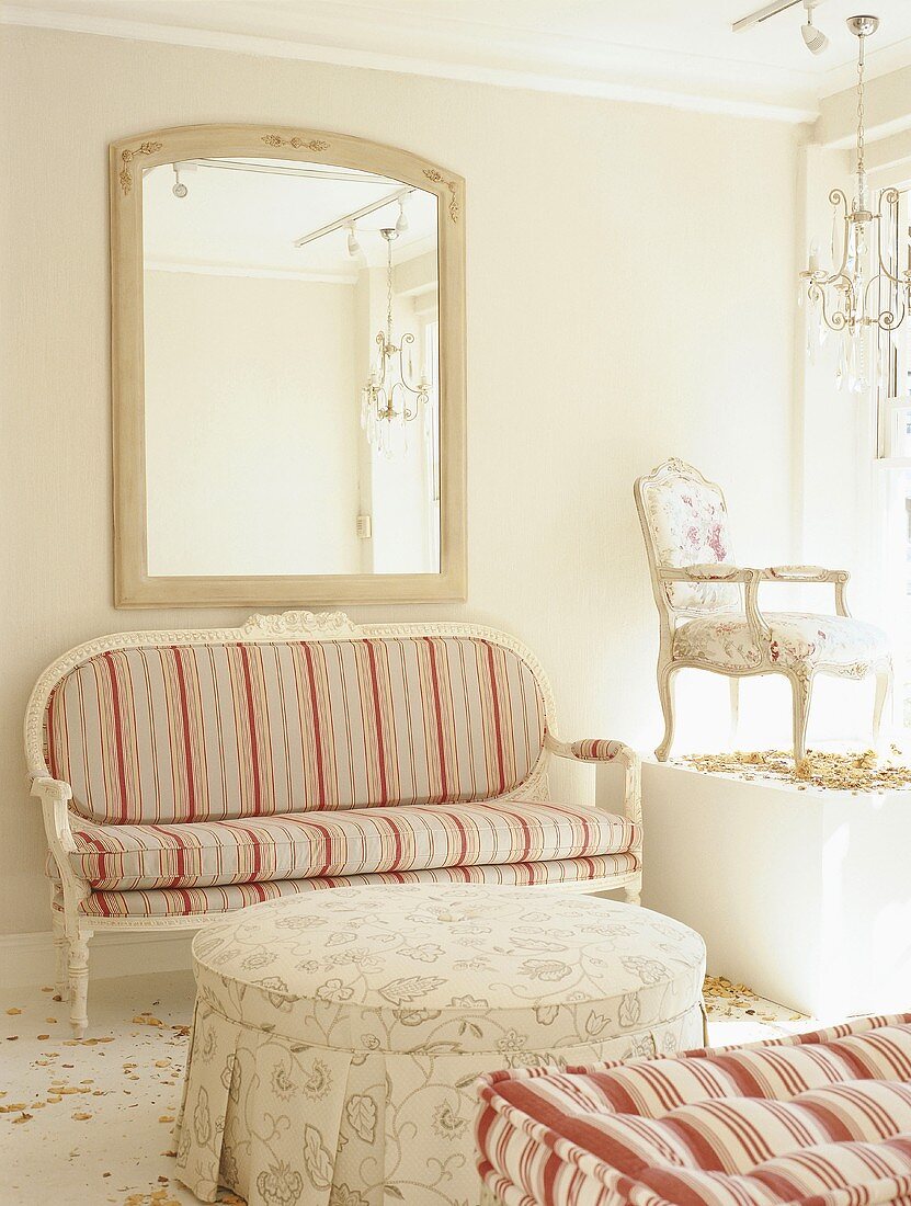 Zierliche Couch mit Streifenmuster im Biedermeierstil unter großem, gerahmten Spiegel; auf einem Podest ein barocker Stuhl