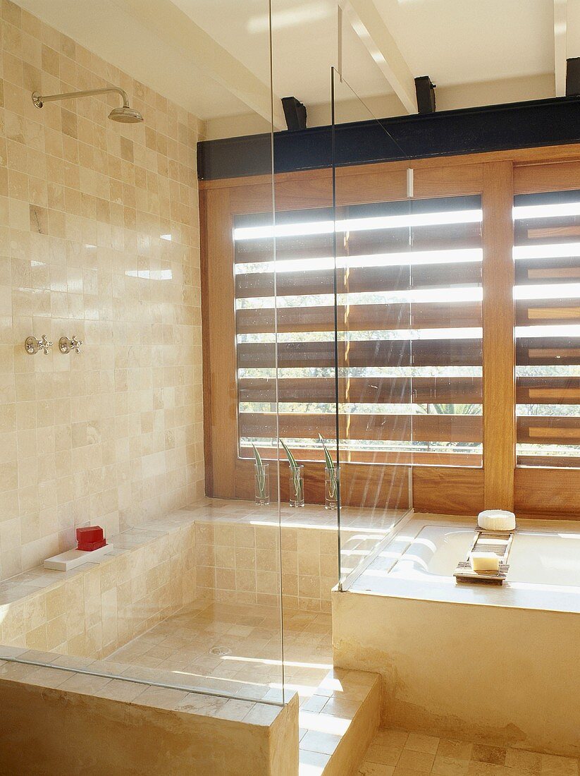 Transparente Duschkabine neben Badewanne vor Fensterläden aus Holz im mediterranem Bad