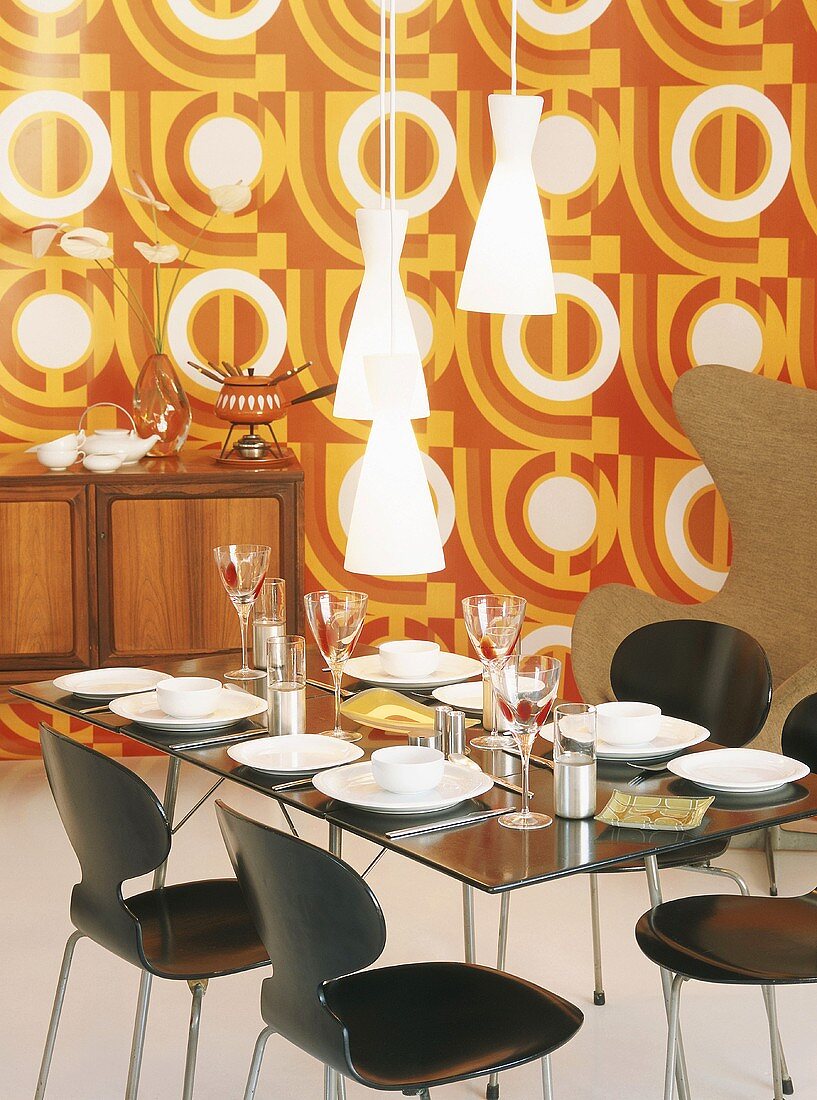Gedeckter Esstisch und Kommode mit Käsefondue-Set vor Wandtapete im 70er Jahre Stil