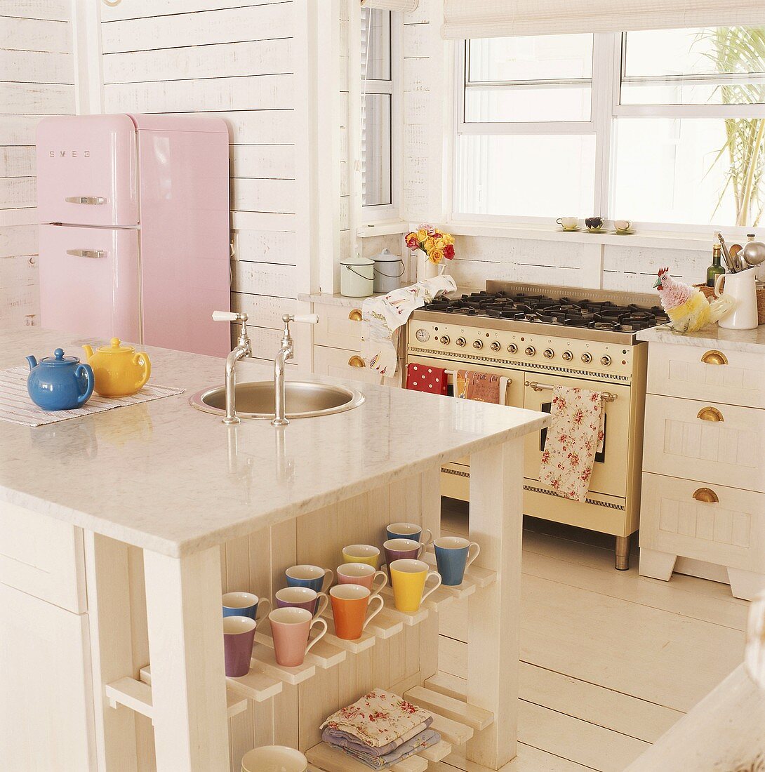 Rustikale Küche mit Gasherd unter dem Fenster, rosa Kühlschrank und Kochinsel mit Stauraum für bunte Tassen