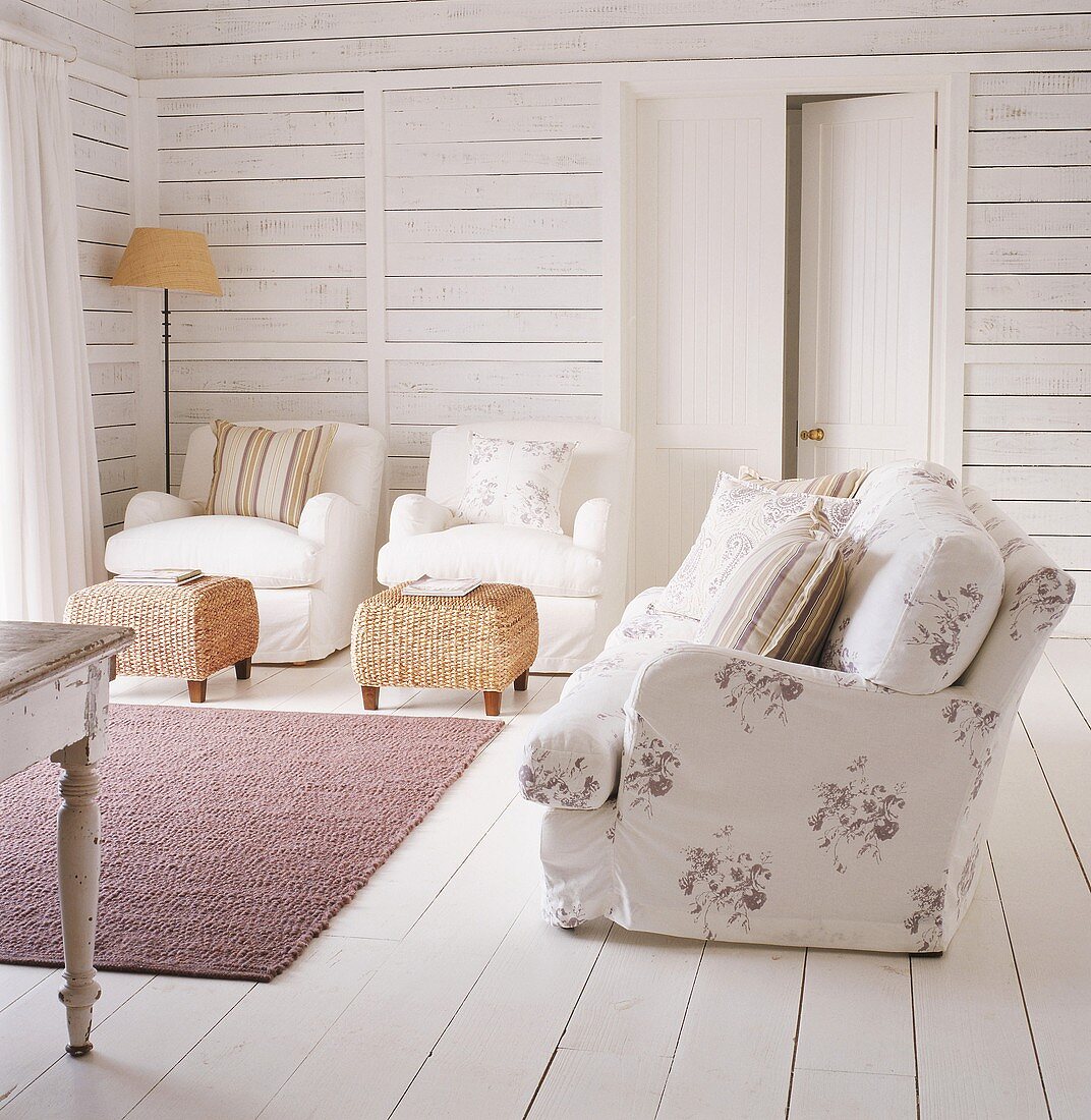 Zwei weiße Sessel und geblümte Couch im maritimen Wohnzimmer mit weiß lackierten Dielenwänden