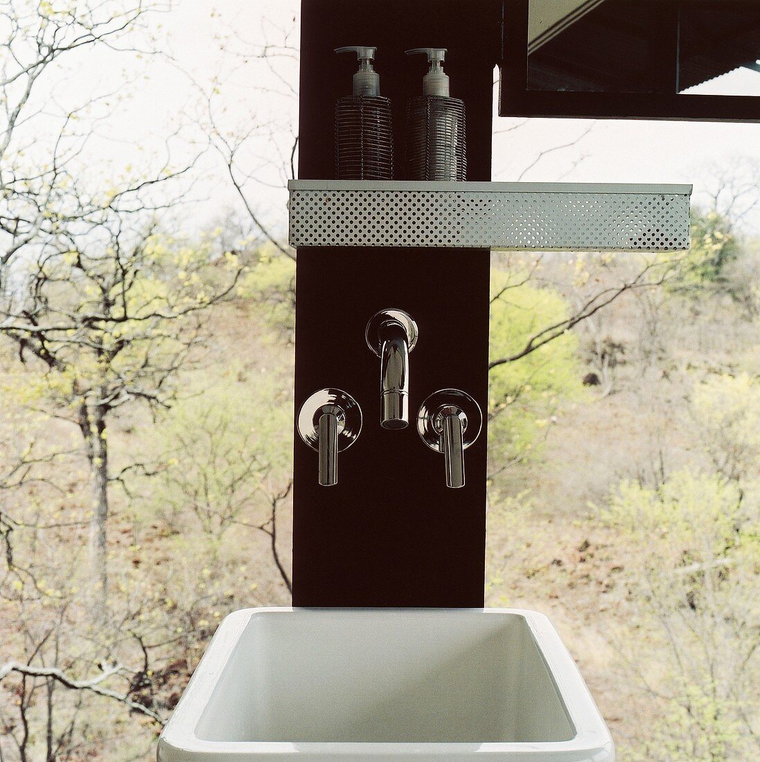 Waschbecken und Armaturen in einer Holzsäule vor Panoramafenster mit Blick auf den Wald