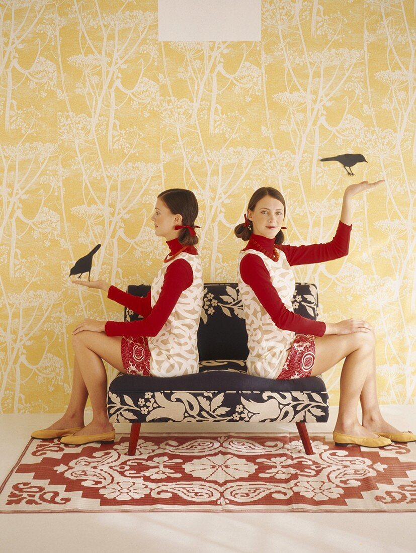 Zwillingspärchen auf einem Sessel mit Schwarzweissmuster vor einer Wand mit Motivtapete