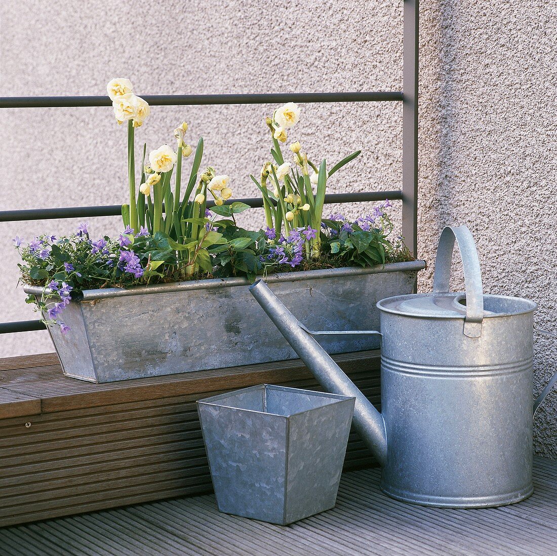 Watering can and flowers in window box on balcony