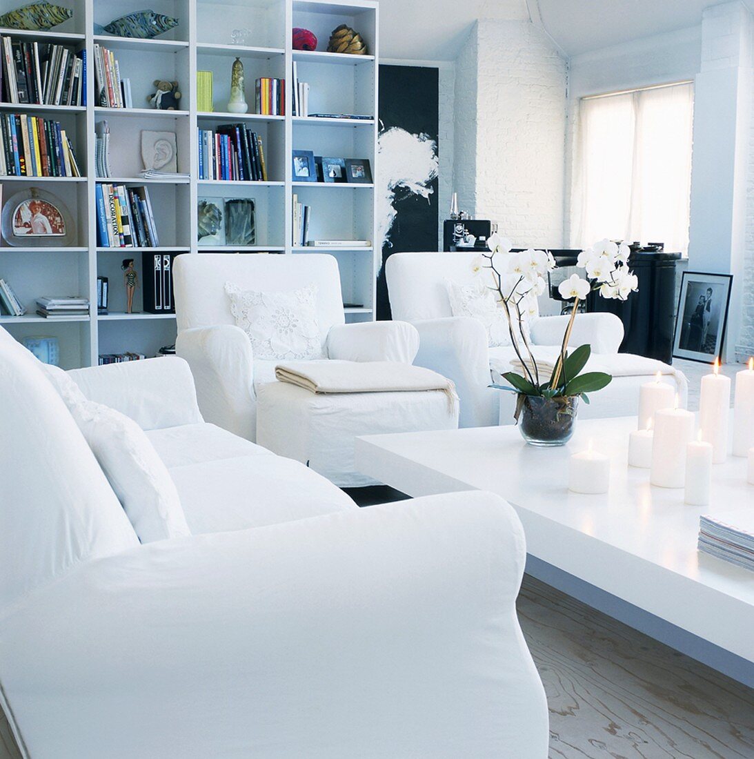 Elegantes Wohnzimmer mit weißer Couchgarnitur, brennenden weißen Kerzen und weiße Orchidee auf Couchtisch