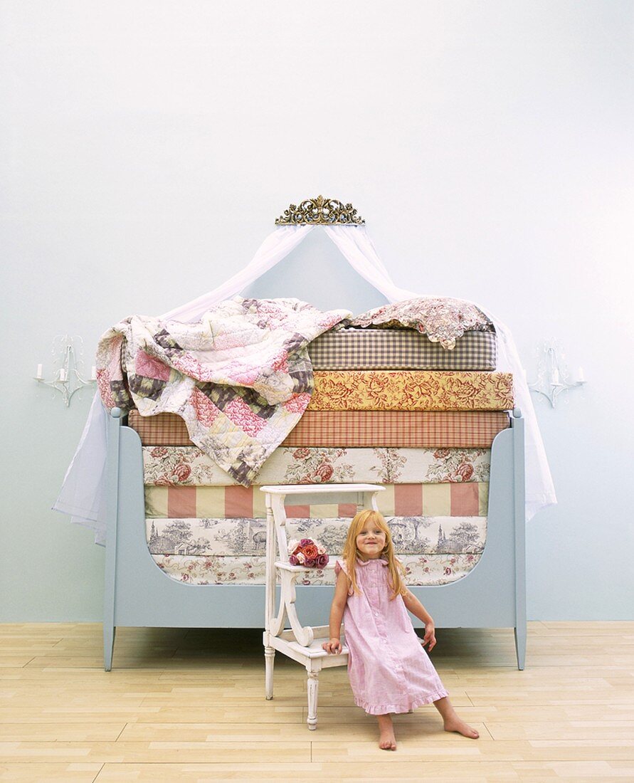 Kleines Mädchen vor Bett mit gestapelten Matratzen sitzend