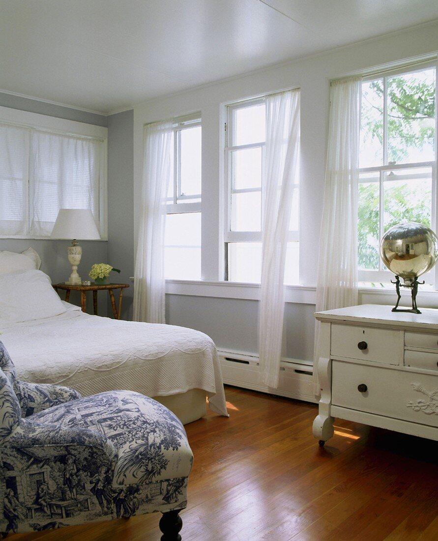 Komfortables Schlafzimmer mit langer Fensterfront und luftigen Chiffonvorhängen