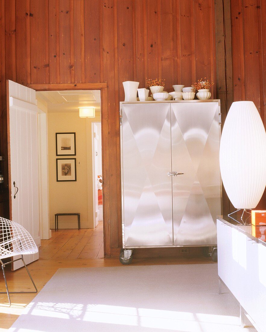 Wohnzimmerschrank mit glänzender Metallfront vor einer holzverkleideten Wand