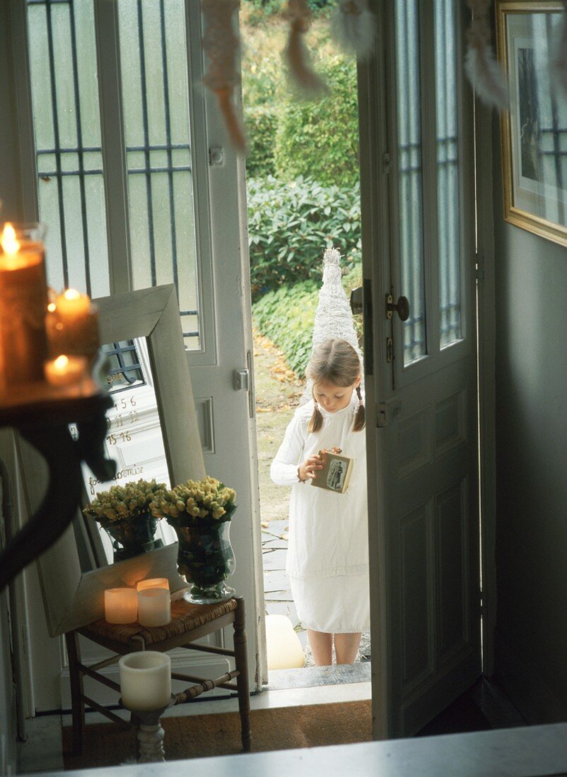 Mädchen in weißem Kleid steht vor der offenen Haustür