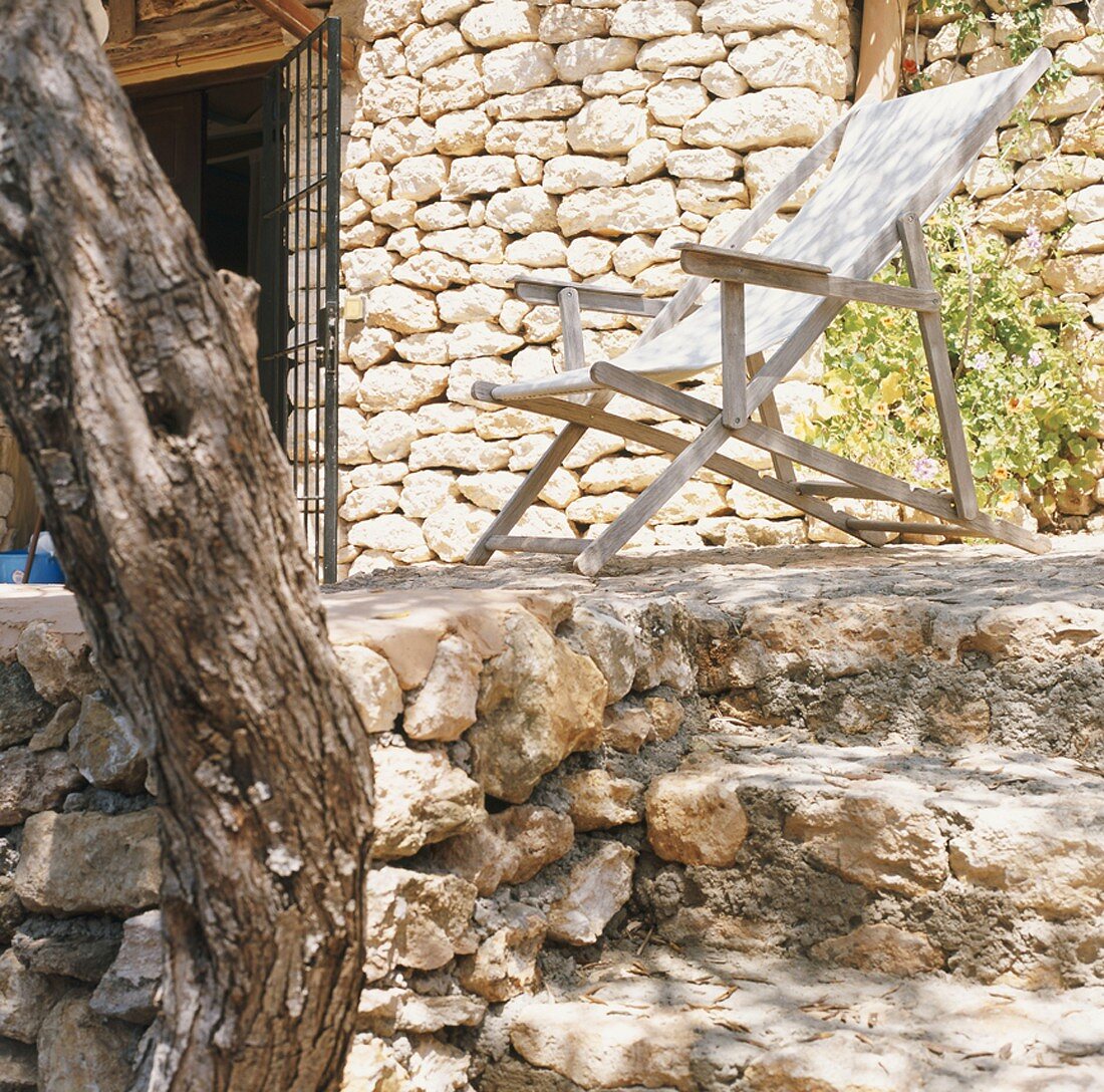 Holzliegestuhl auf Terrasse vor Steinfassade mit Treppenstufen