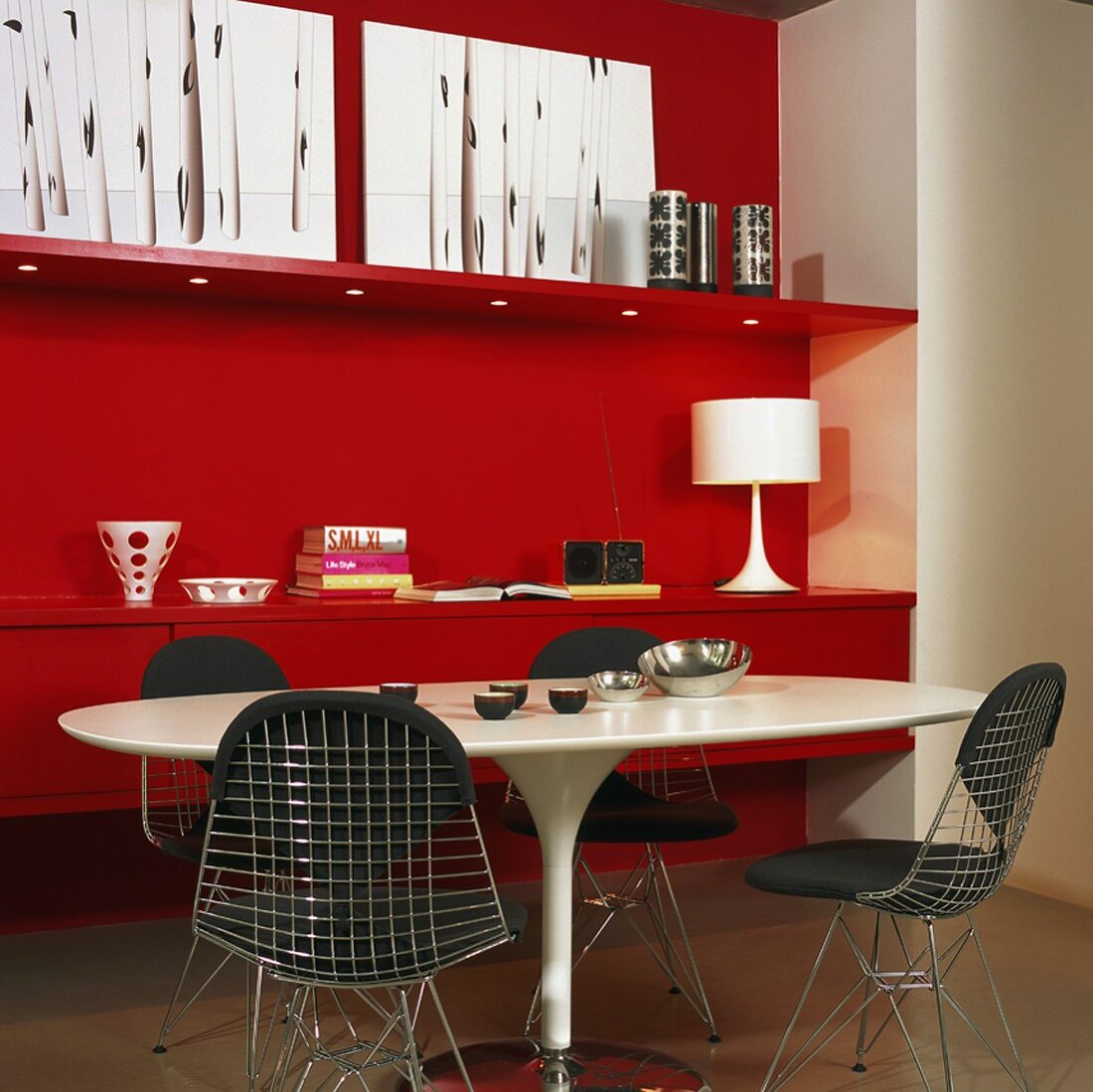 Rote Wand mit rotem Sideboard; davor ein weisser Tisch mit schwarzgepolsterten Metallstühlen