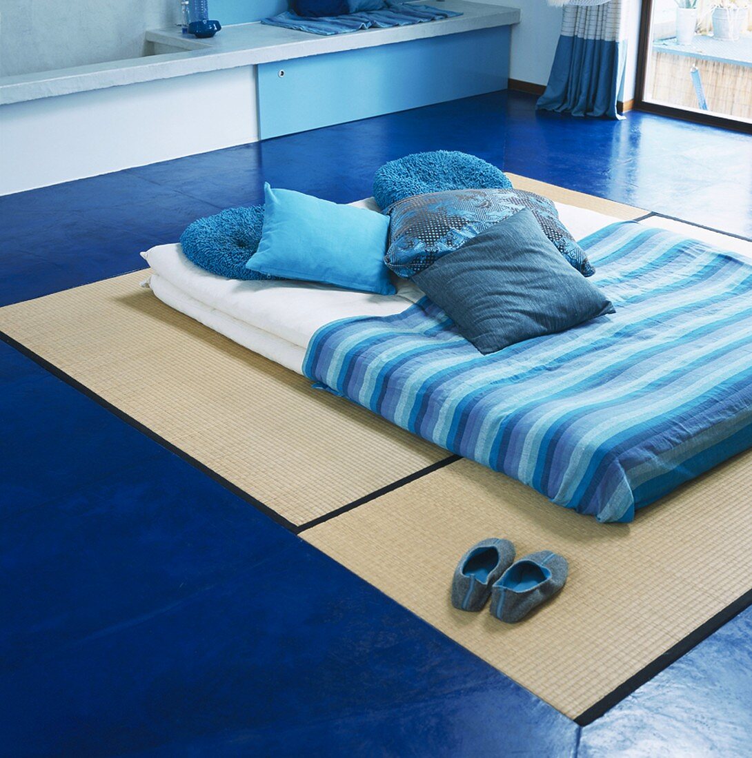 Futon with blue scatter cushions & blue blanket on tatami mats on floor