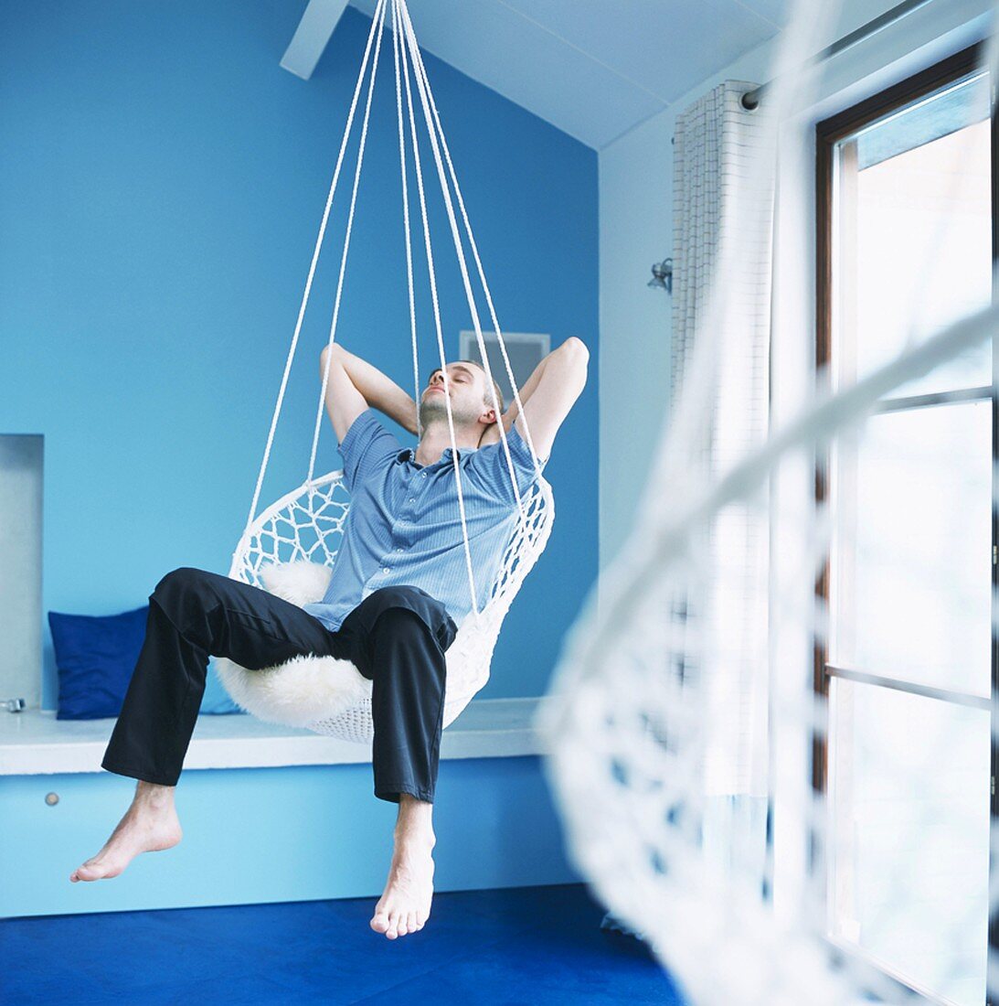 Man relaxing in hanging chair in blue bedroom