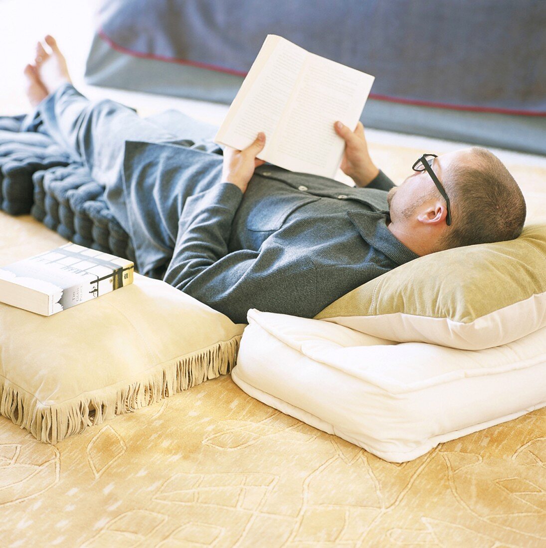 Man lying on floor cushions reading book