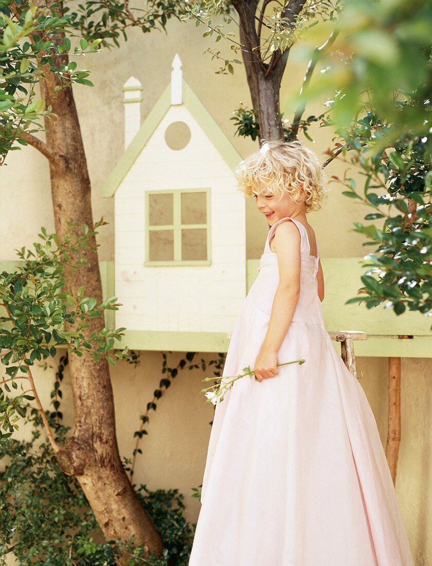 Kleines Mädchen mit langem, rosa Kleid im Garten