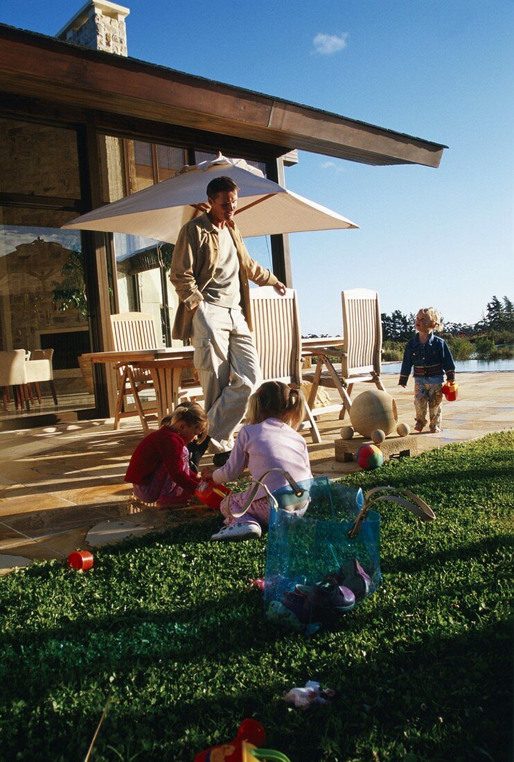 Vater mit drei spielenden Kindern auf Terrasse vor Wohnhaus