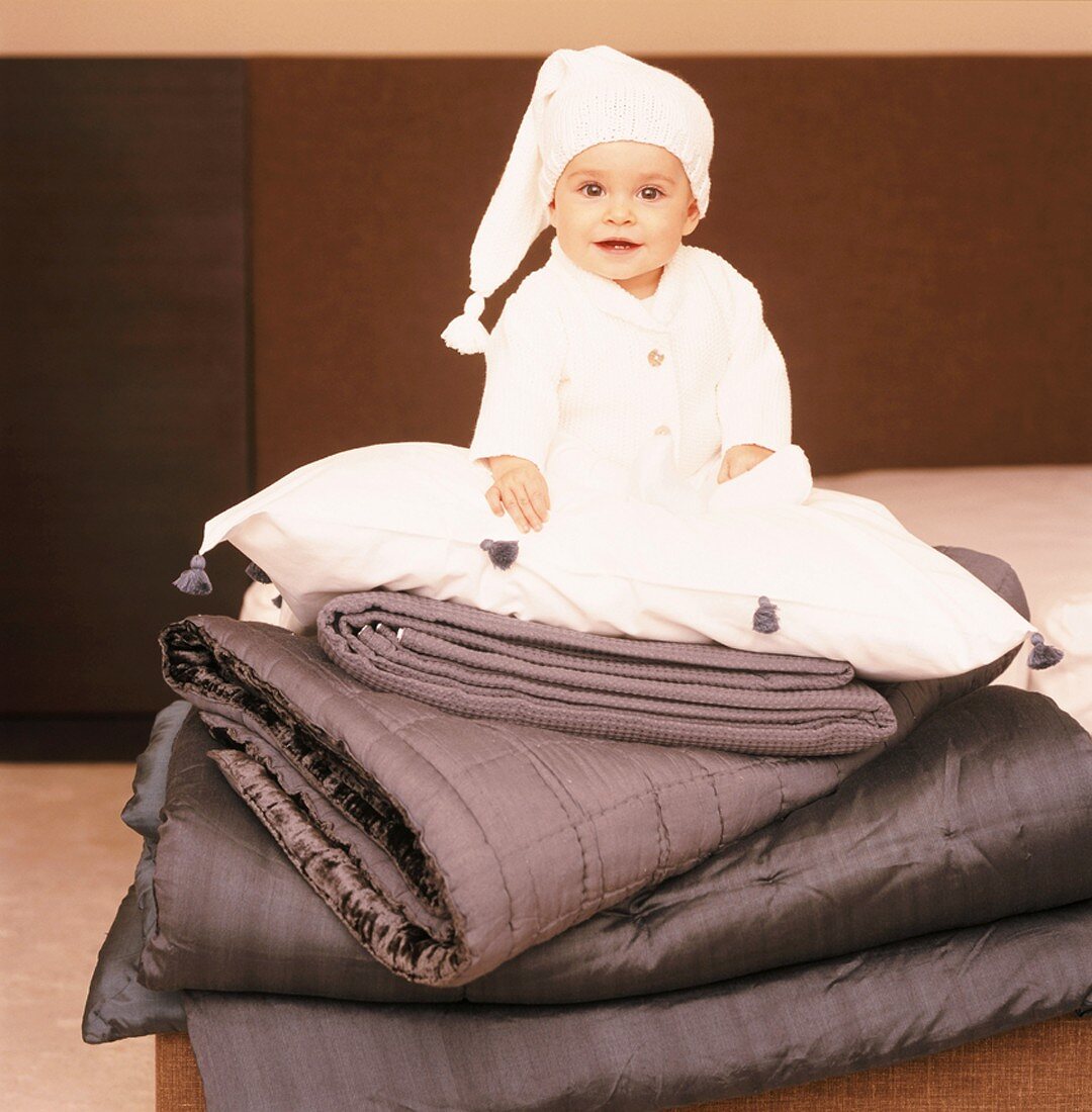 Baby mit Mütze auf einem Stapel Decken
