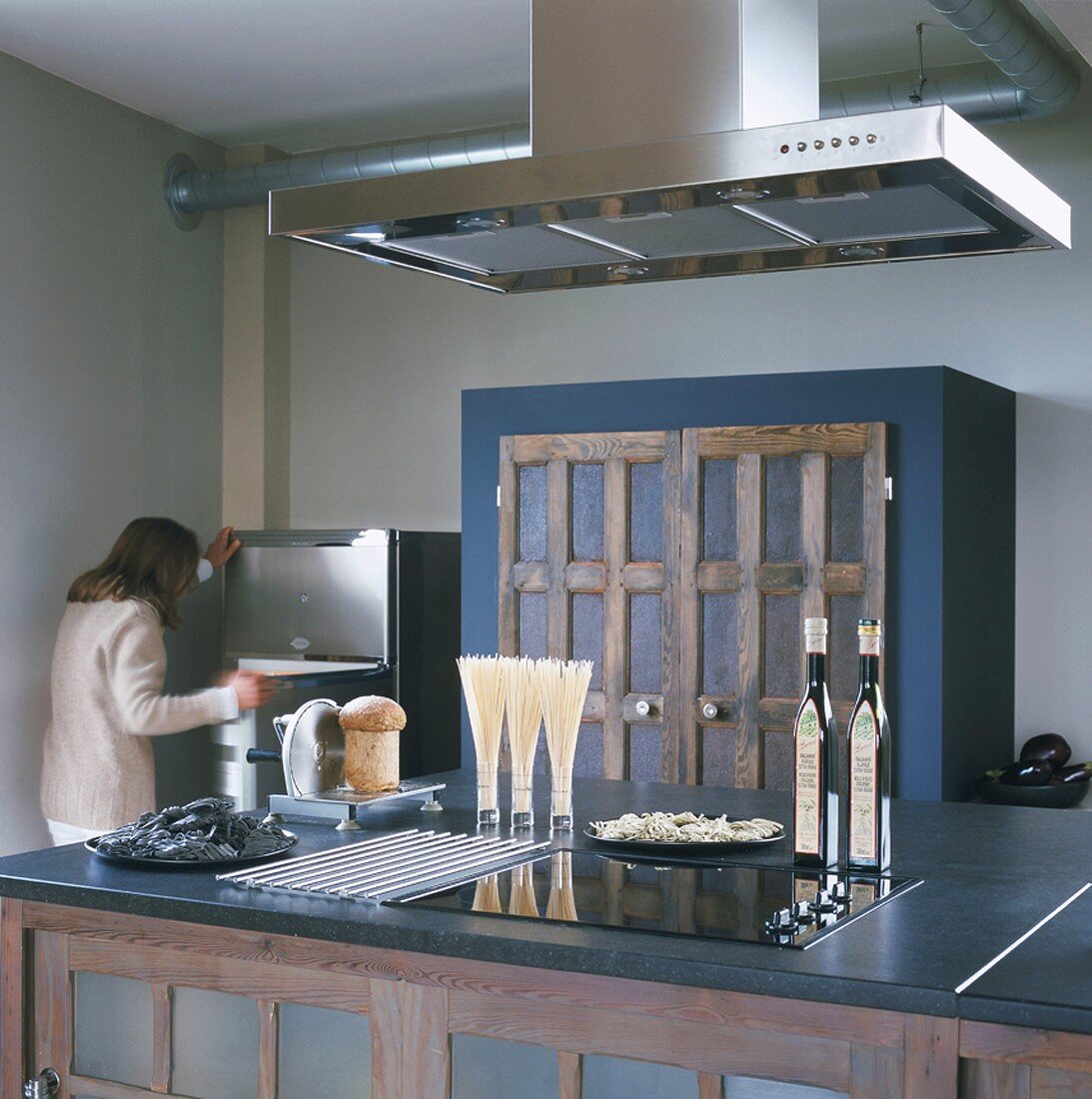 Woman opening fridge behind kitchen counter with hob