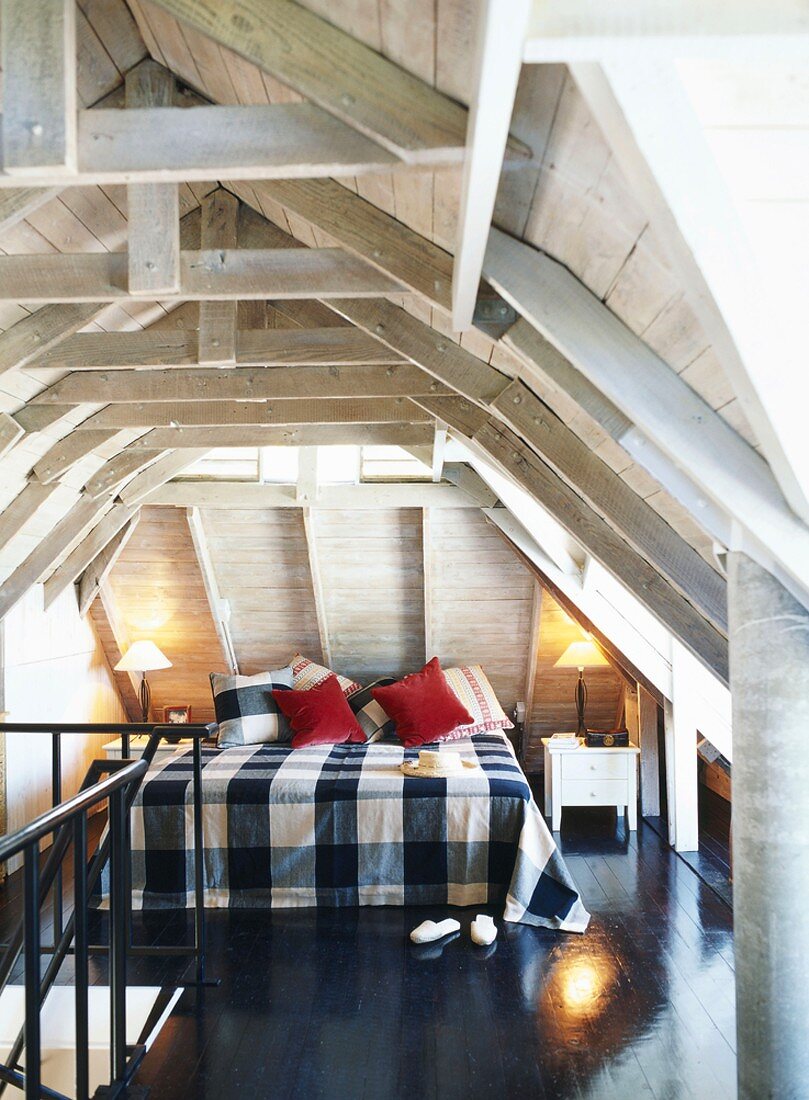 Großes Doppelbett mit karierter Tagesdecke in Dachgeschossschlafzimmer mit heller Holzbalkendecke