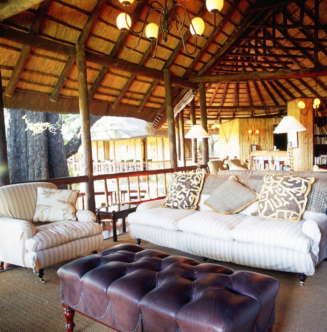 Offener Wohnbereich mit gemütlichem Sofa und Sessel unter einem Reetdach in der Natur
